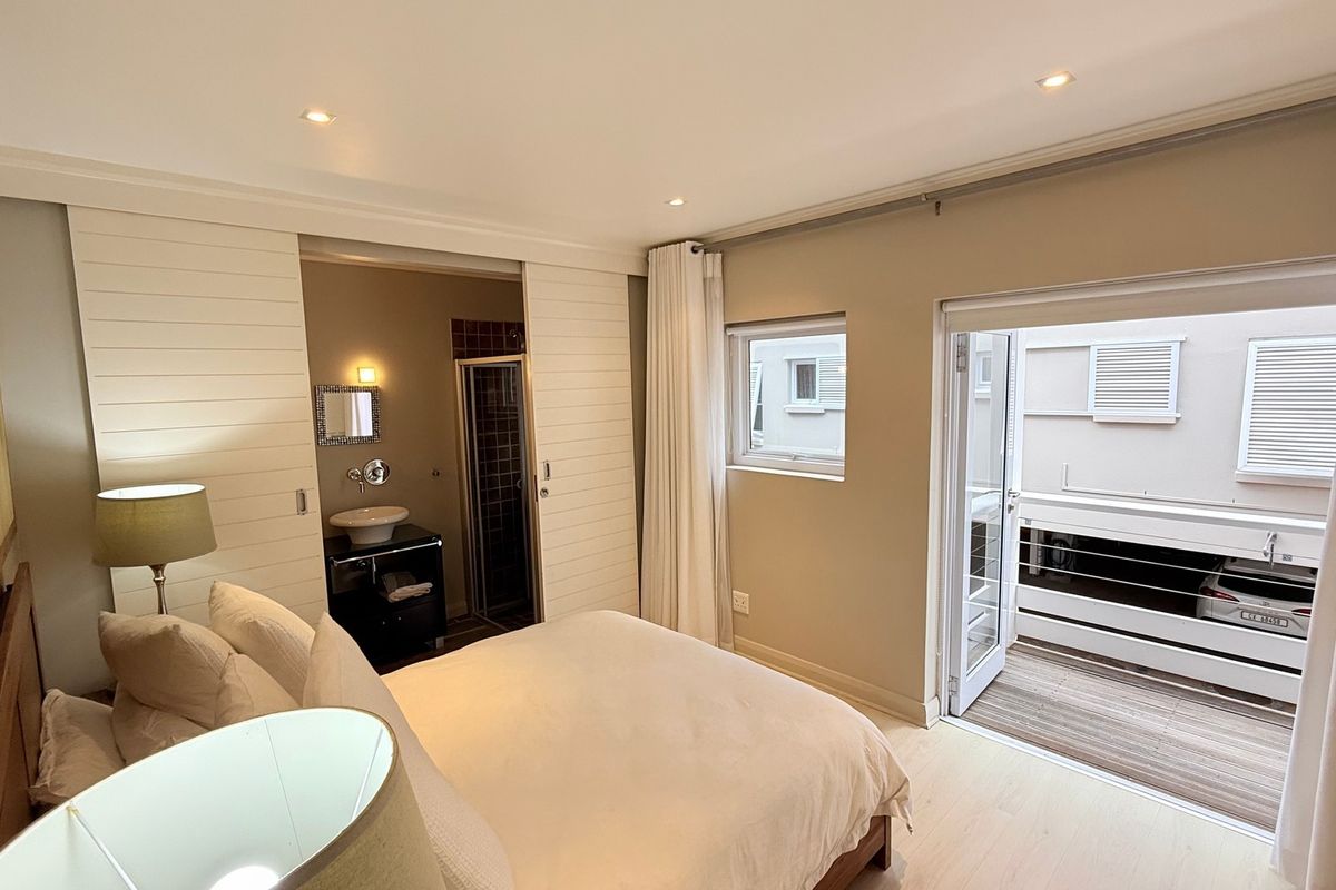 A well-maintained bedroom featuring an en-suite bathroom, recessed lighting, and direct access to a private balcony with timber decking.