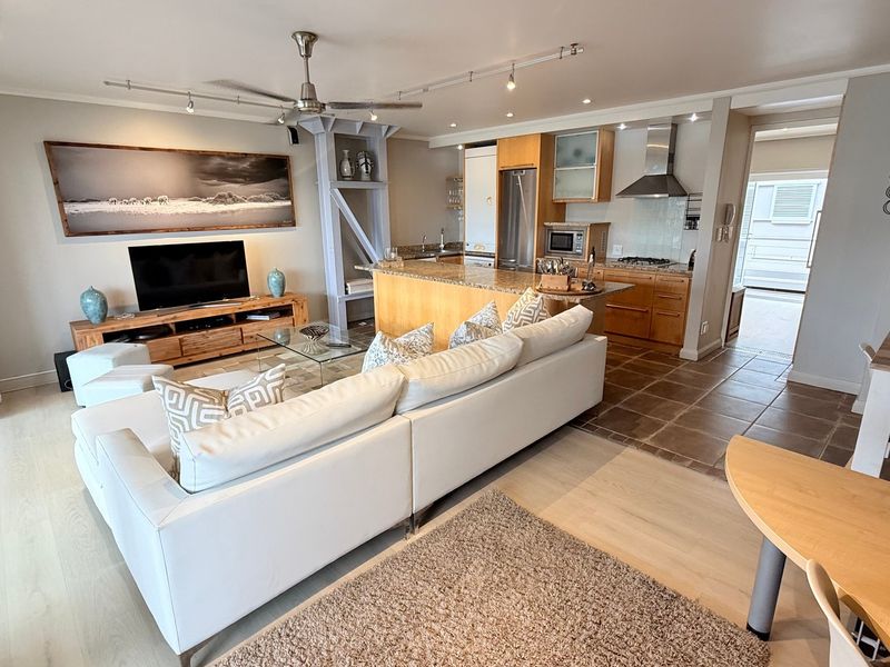 Spacious open-plan living area featuring a modern kitchen with granite countertops, wooden cabinetry, and integrated appliances, flowing into a comfortable lounge space.
