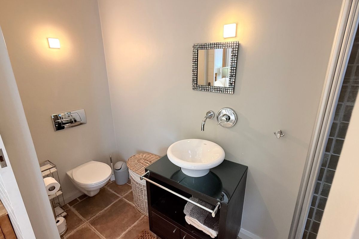 A modern bathroom featuring a wall-mounted toilet, a sleek vessel sink on a dark vanity cabinet, and contemporary wall-mounted fixtures.