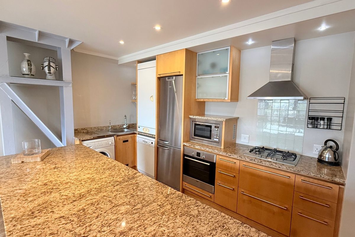 A well-equipped kitchen featuring granite countertops, wooden cabinetry, built-in appliances including an oven, gas hob, and integrated dishwasher, with recessed lighting.