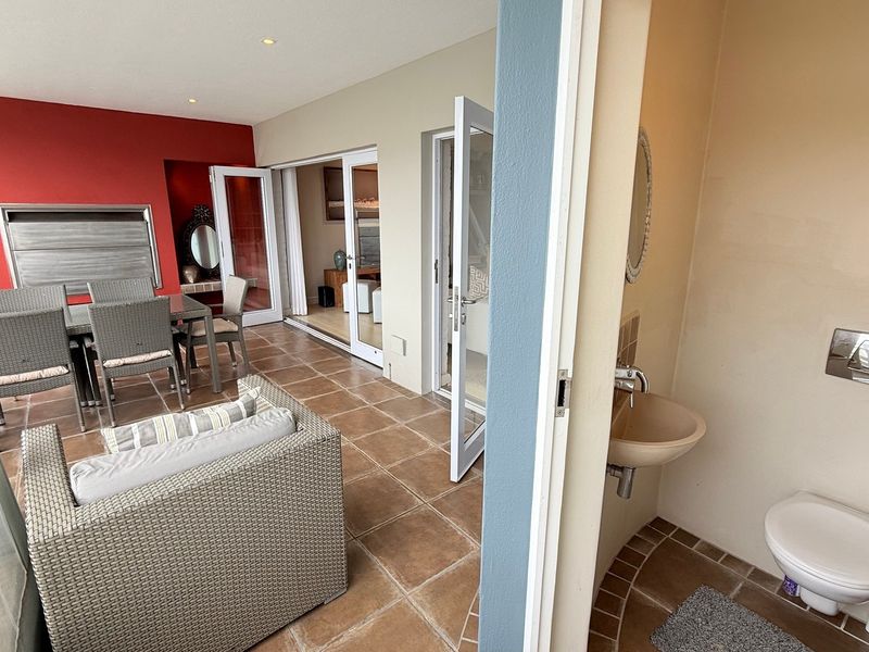 A covered patio area featuring tiled flooring, recessed lighting, and a built-in braai, with an adjacent small guest bathroom containing a wall-mounted toilet and basin.