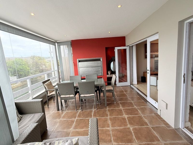 Covered balcony featuring tiled flooring, a built-in braai, and glass enclosure, providing a versatile outdoor entertainment space with access to the interior.