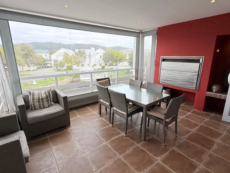 Covered balcony featuring tiled flooring, a built-in braai, and glass balustrades with views, offering a versatile outdoor entertainment space.