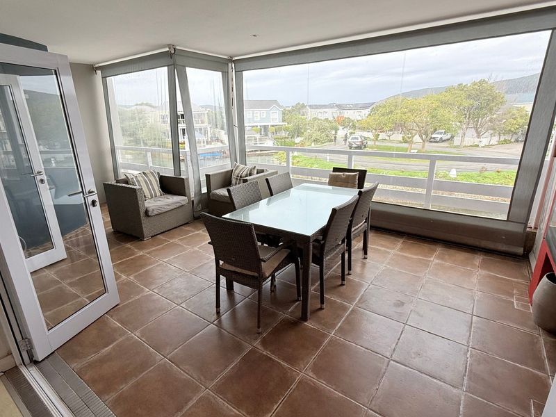 Enclosed balcony featuring tiled flooring, large glass panels, and a railing, offering a versatile outdoor living space with neighborhood views.