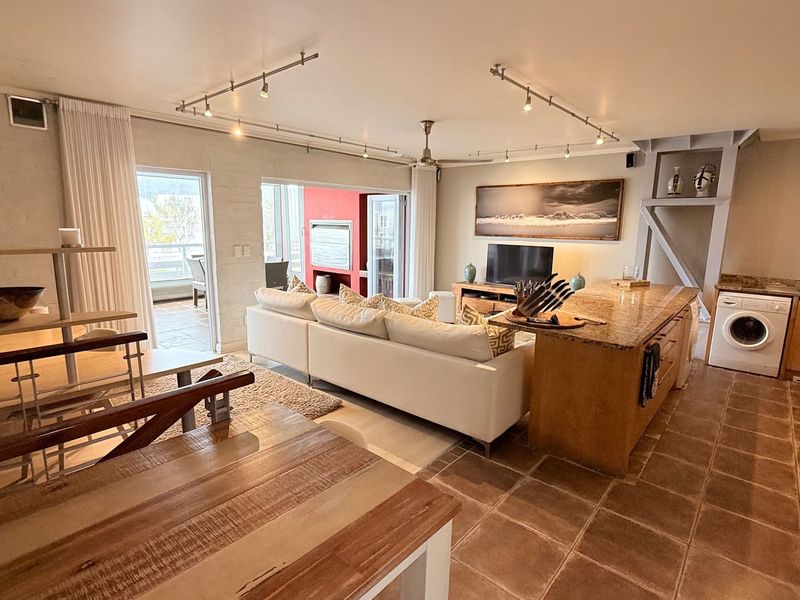 Spacious open-plan living area featuring a kitchen with granite island, integrated appliances, tiled flooring, and direct access to a balcony through sliding glass doors.
