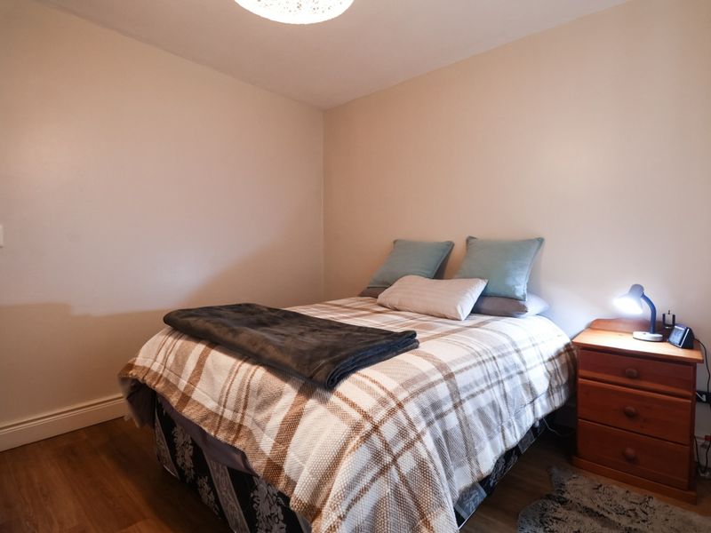 A functional bedroom featuring laminate flooring, neutral wall finishes, and standard electrical fixtures, providing a clean and simple living space.