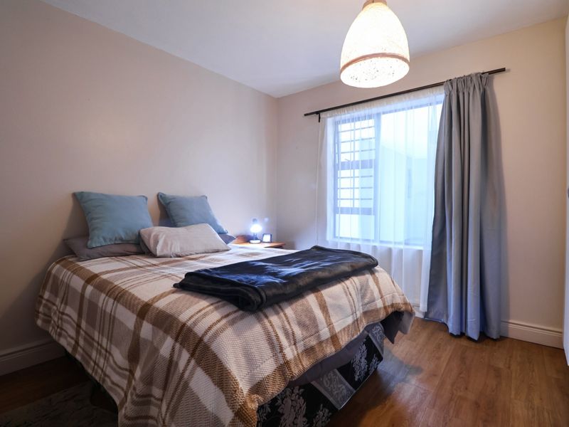 A well-maintained bedroom featuring laminate flooring, a built-in wardrobe, and a window with curtain fixtures, offering a comfortable and functional living space.
