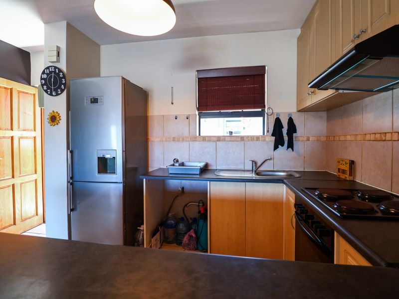 Functional kitchen featuring laminate cabinetry, dark countertops, integrated electric hob, extractor fan, and a tiled backsplash with a window for natural light.