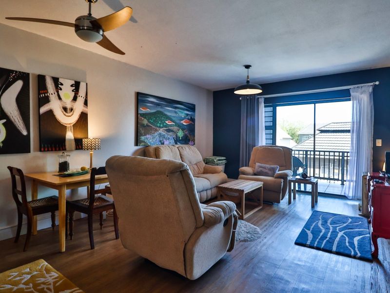 A comfortable living room featuring laminate flooring, a ceiling fan, and a sliding glass door providing access to an outdoor balcony area.