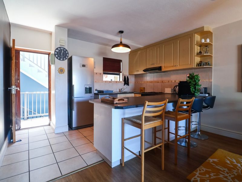 Open plan kitchen featuring a breakfast bar, wooden cabinetry, and tiled flooring, with direct access to an external balcony area.