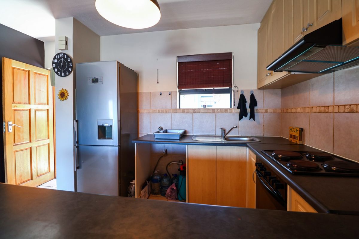 Functional kitchen featuring laminate cabinetry, dark countertops, integrated electric hob, extractor fan, and a tiled backsplash with a window for natural light.