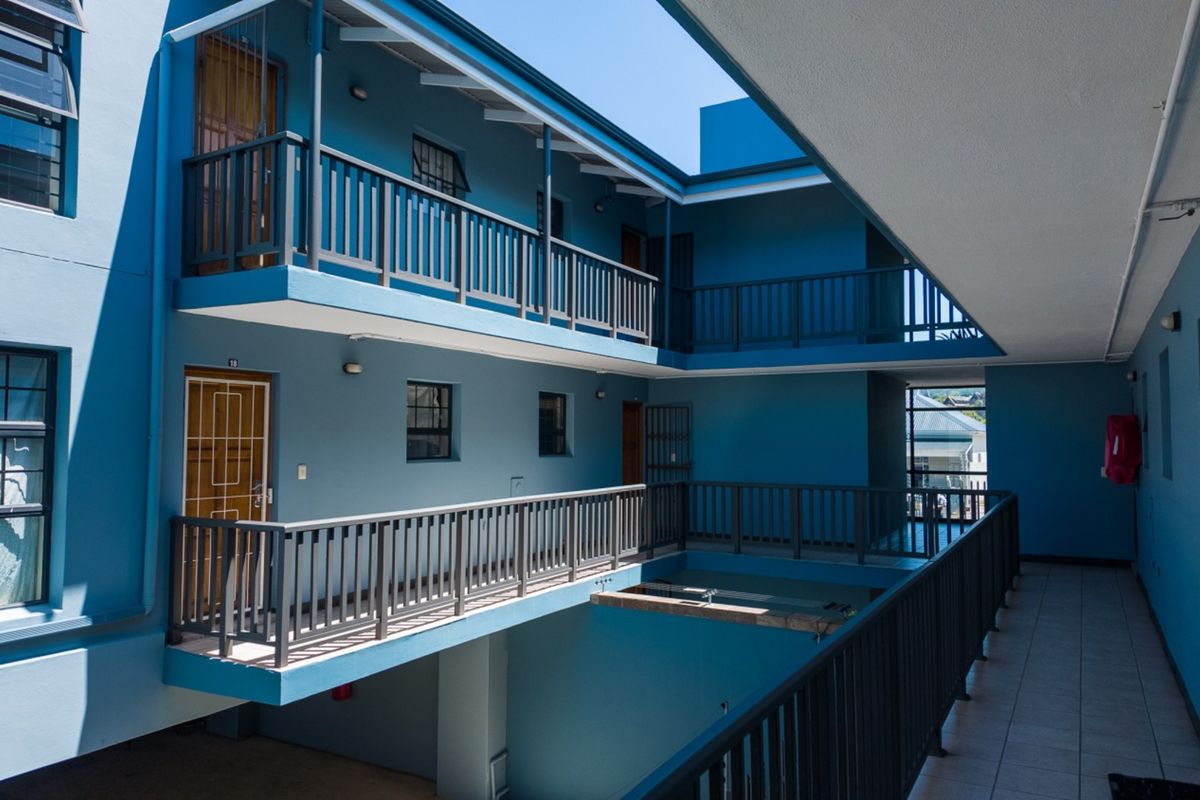 An exterior view of an apartment complex featuring open-air walkways, balcony railings, and security gates on multiple levels.