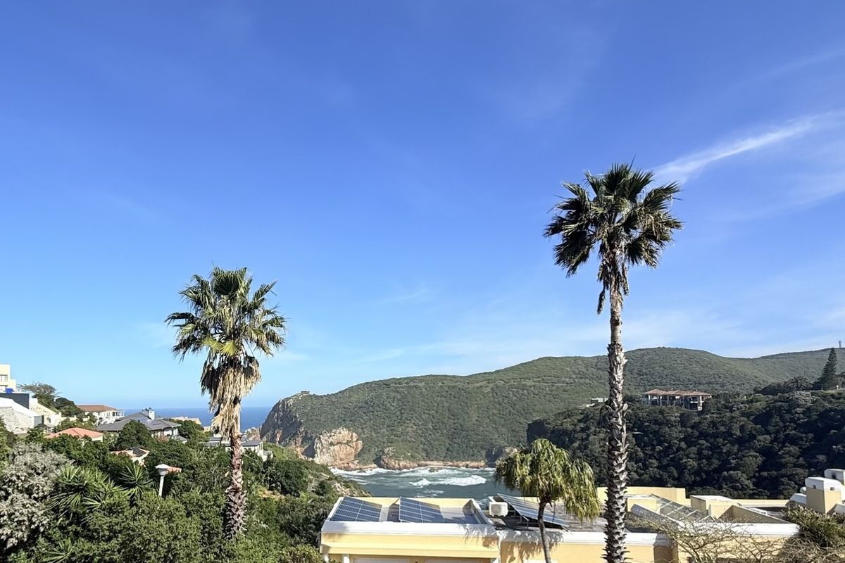 A scenic elevated view overlooking the coastline, lush green hills, and the ocean, featuring solar panels installed on the nearby roof.