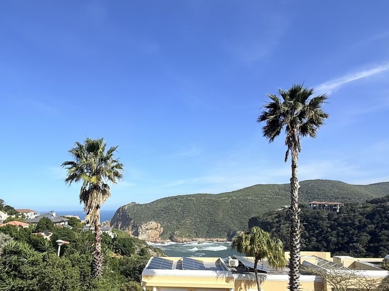 A scenic elevated view overlooking the coastline, lush green hills, and the ocean, featuring solar panels installed on the nearby roof.