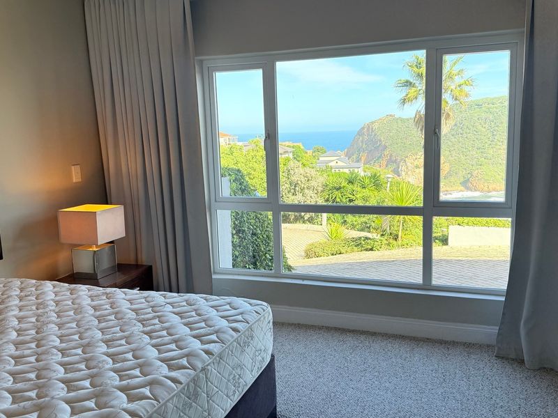 A bright bedroom featuring a large picture window with scenic coastal and landscape views, neutral carpeting, and integrated curtain tracks.