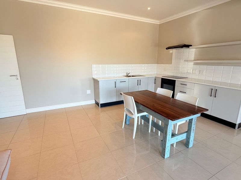 Open-plan kitchen and dining area featuring modern white cabinetry, tiled flooring, built-in cooktop, and a clean, neutral aesthetic.