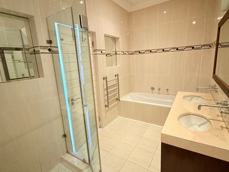 A well-maintained bathroom featuring a double vanity, built-in bathtub, glass-enclosed shower, and neutral tiled finishes throughout.