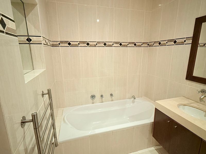 A clean, well-maintained bathroom featuring a built-in bathtub, stone-topped vanity with undermount sink, and a wall-mounted heated towel rail.