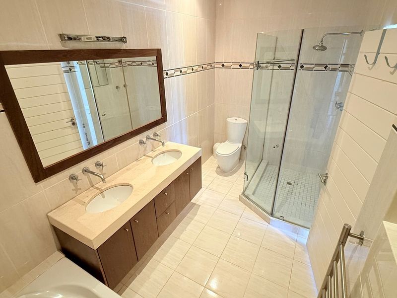 A well-maintained bathroom featuring a double vanity with stone countertop, a glass-enclosed shower, and a heated towel rail.