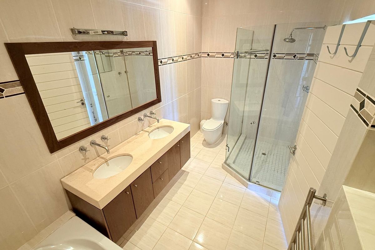 A well-maintained bathroom featuring a double vanity with stone countertop, a glass-enclosed shower, and a heated towel rail.