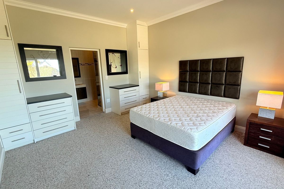 Spacious bedroom featuring neutral walls, carpeted flooring, built-in cupboards, and direct access to an en-suite bathroom.