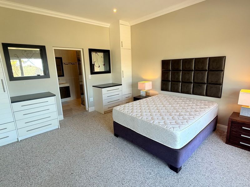Spacious bedroom featuring neutral walls, carpeted flooring, built-in cupboards, and direct access to an en-suite bathroom.