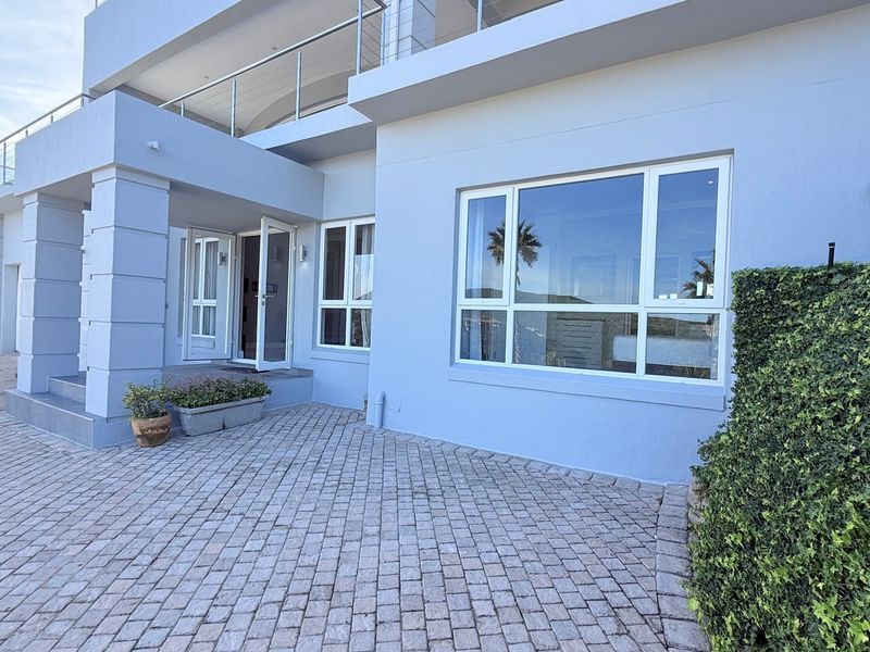 A well-maintained front exterior view of the apartment building featuring paved driveway, modern aluminum window frames, and a balcony with metal railing.