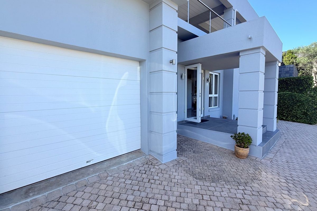 Front elevation of the apartment featuring a paved driveway, a white sectional garage door, and a covered entrance porch with an overhead balcony.