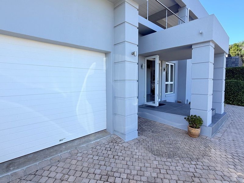 Front elevation of the apartment featuring a paved driveway, a white sectional garage door, and a covered entrance porch with an overhead balcony.