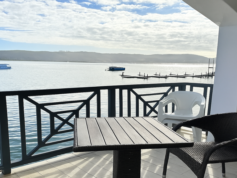 A covered balcony featuring a dark railing and tiled flooring, offering expansive views over the water.