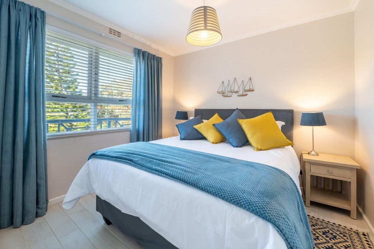A well-maintained bedroom featuring a large window with venetian blinds, neutral wall finishes, and decorative coving.