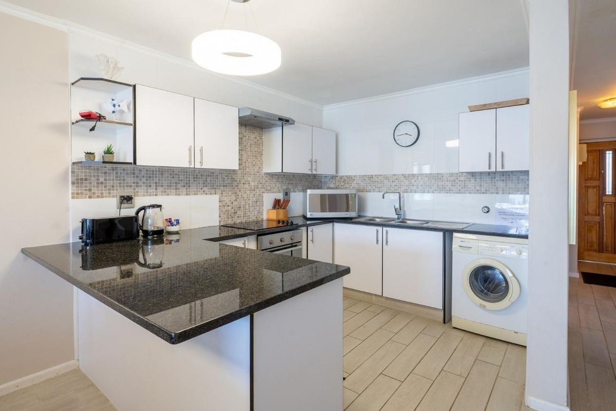 A functional kitchen featuring white cabinetry, granite countertops, a tiled backsplash, and integrated appliances including an oven, hob, and extractor fan.