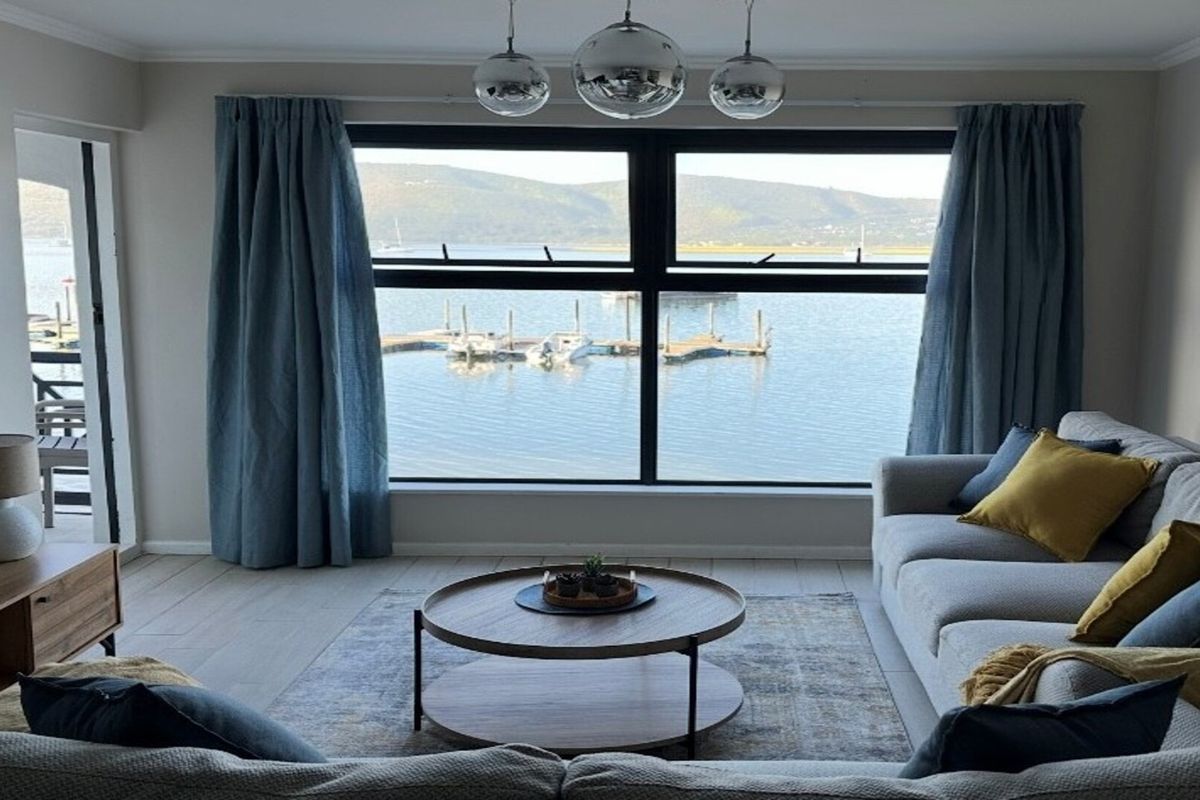 A bright living room featuring a large picture window with scenic water views, tiled flooring, and modern pendant lighting.