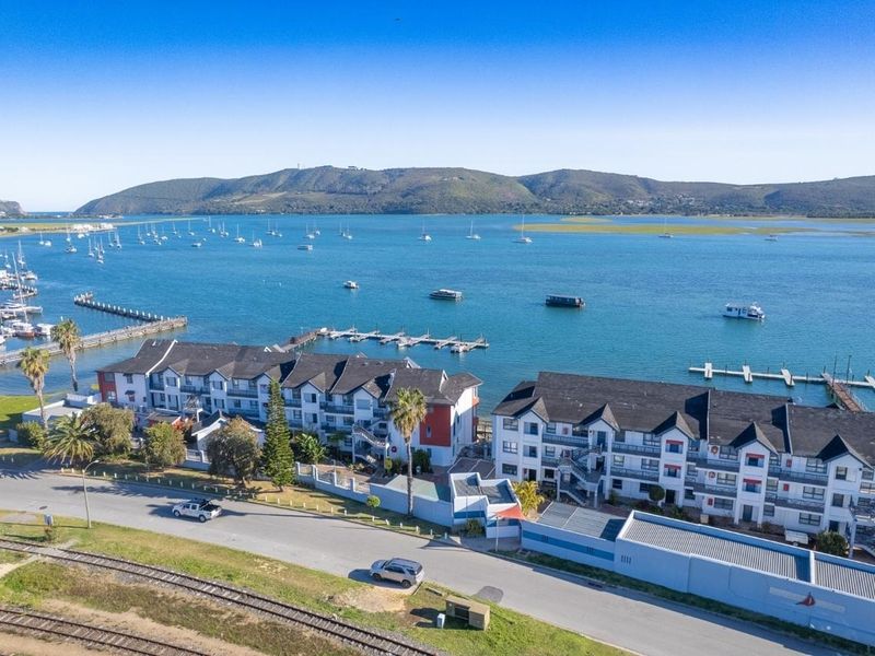 Aerial view of a waterfront apartment complex featuring multiple buildings, balconies, and direct access to a jetty and the lagoon.