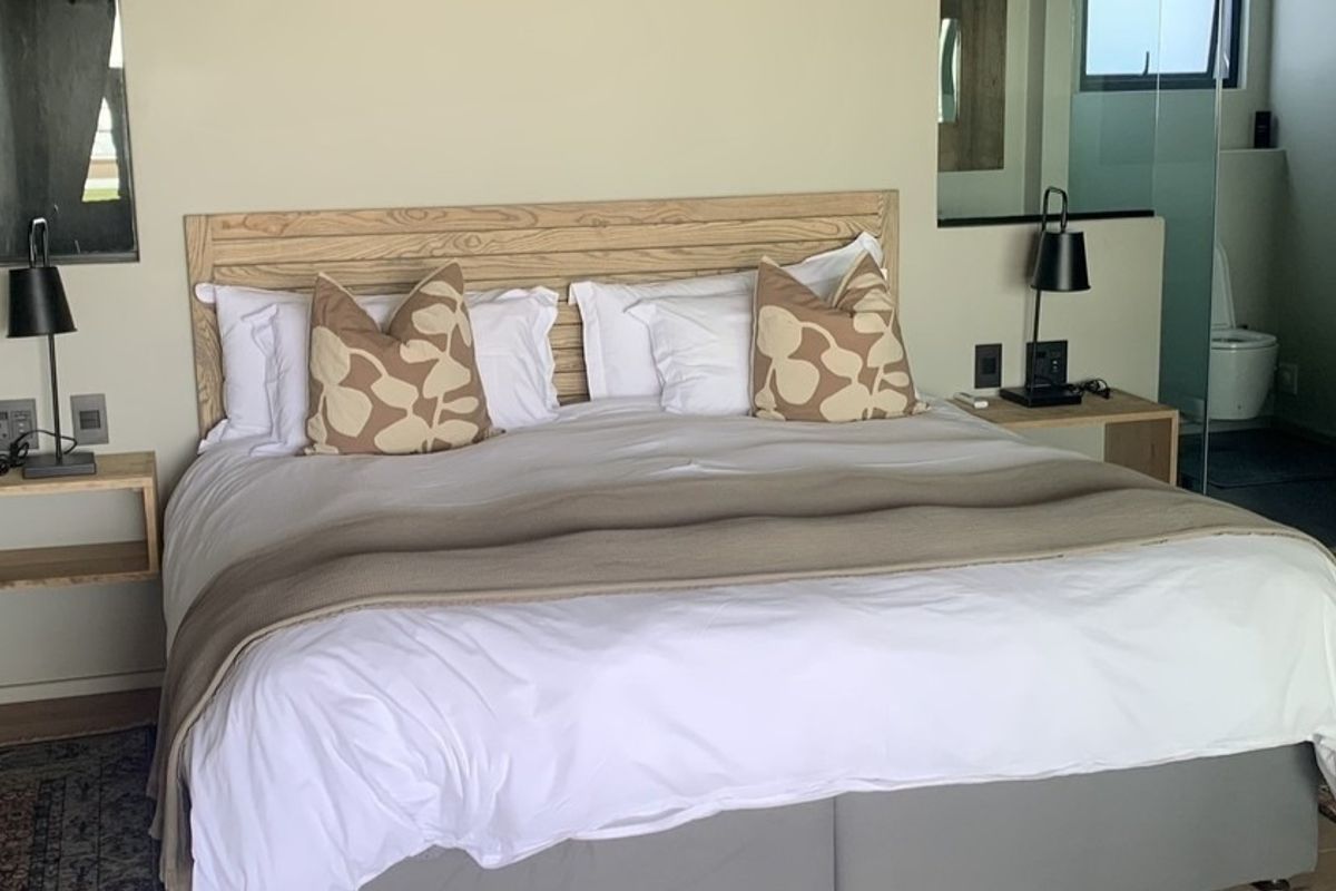 A well-appointed bedroom featuring a modern headboard, integrated bedside shelving, and an open-plan en-suite bathroom with a glass partition.