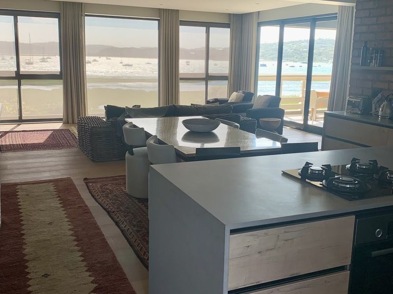 Spacious open-plan living and kitchen area featuring a modern island with gas hob, exposed brick accents, and expansive sliding doors showcasing panoramic water views.