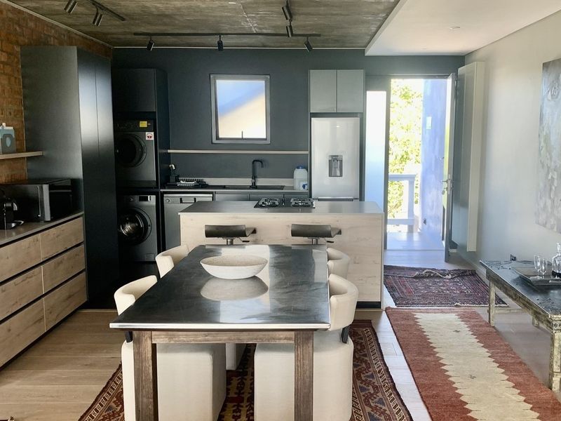 Modern open-plan kitchen and dining area featuring exposed brickwork, concrete ceilings, and a central island with integrated appliances and sleek cabinetry.