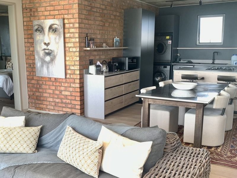 Modern open-plan living area featuring an exposed brick feature wall, contemporary kitchen with integrated appliances, and a seamless flow to the dining space.