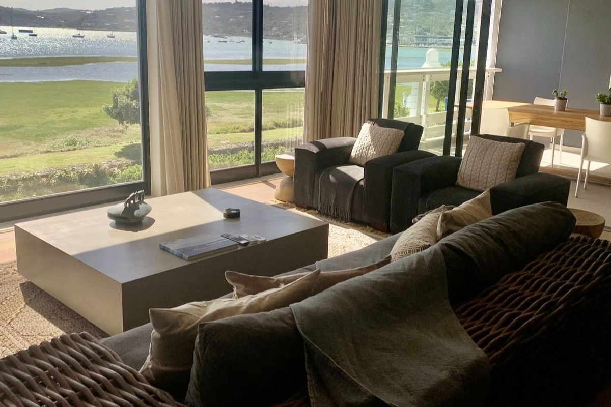Spacious open-plan living area featuring large floor-to-ceiling windows and sliding doors that offer expansive views of the water and landscape.