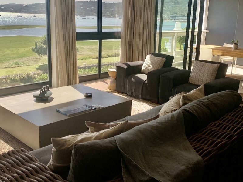 Spacious open-plan living area featuring large floor-to-ceiling windows and sliding doors that offer expansive views of the water and landscape.
