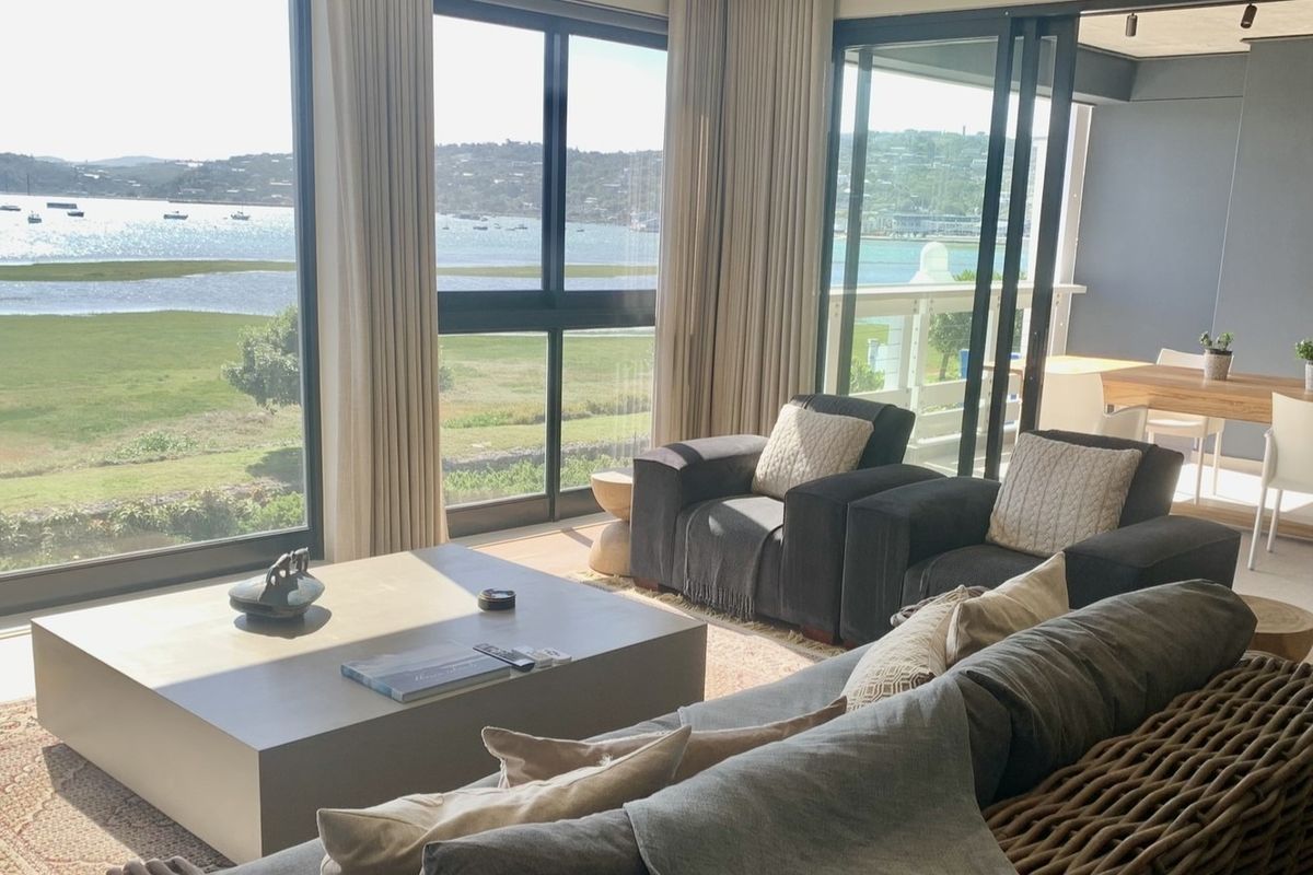 Spacious open-plan living area featuring expansive floor-to-ceiling windows and sliding doors that provide panoramic water views and seamless access to the balcony.