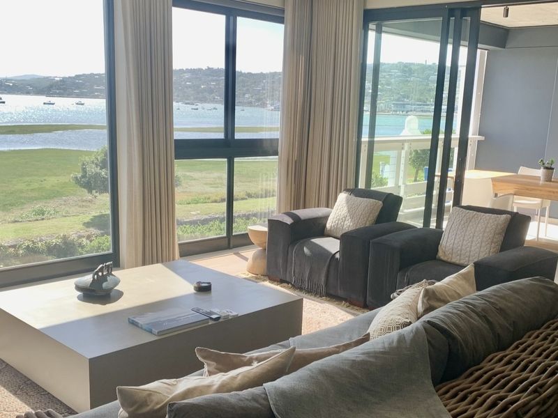 Spacious open-plan living area featuring expansive floor-to-ceiling windows and sliding doors that provide panoramic water views and seamless access to the balcony.