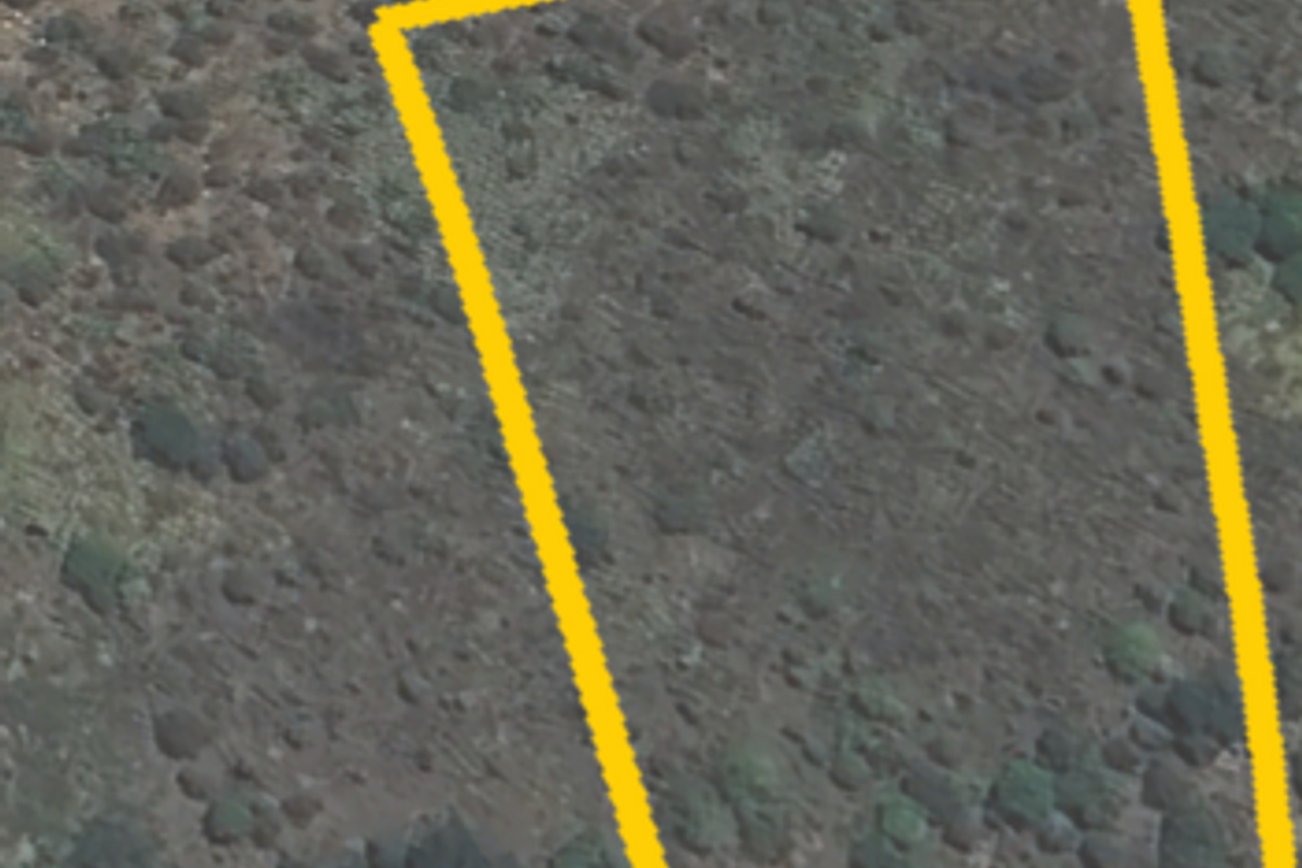 An aerial view of a vacant residential plot of land, highlighting the property boundaries and natural vegetation.