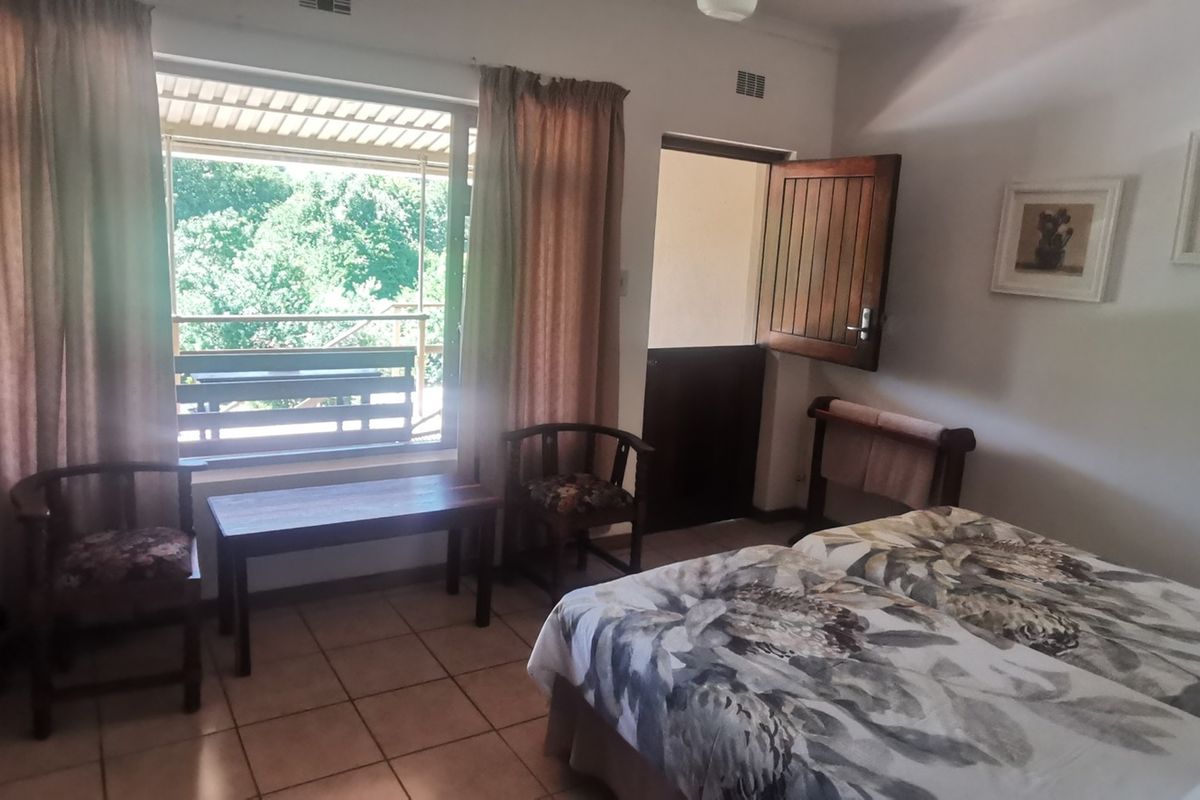 A bedroom featuring tiled flooring, a large window with garden views, and a wooden door leading to an outdoor area.