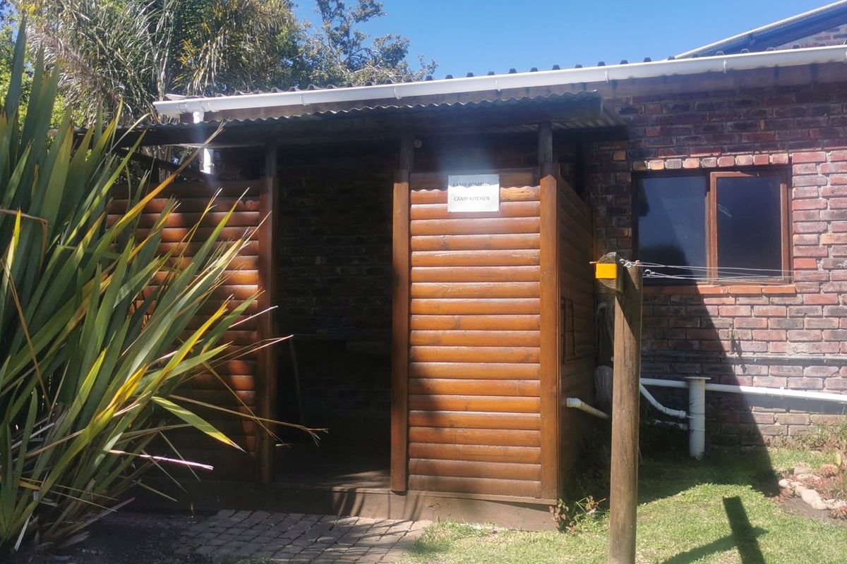 A rustic outdoor camp kitchen area featuring timber cladding and brick construction, situated adjacent to the main farm building.