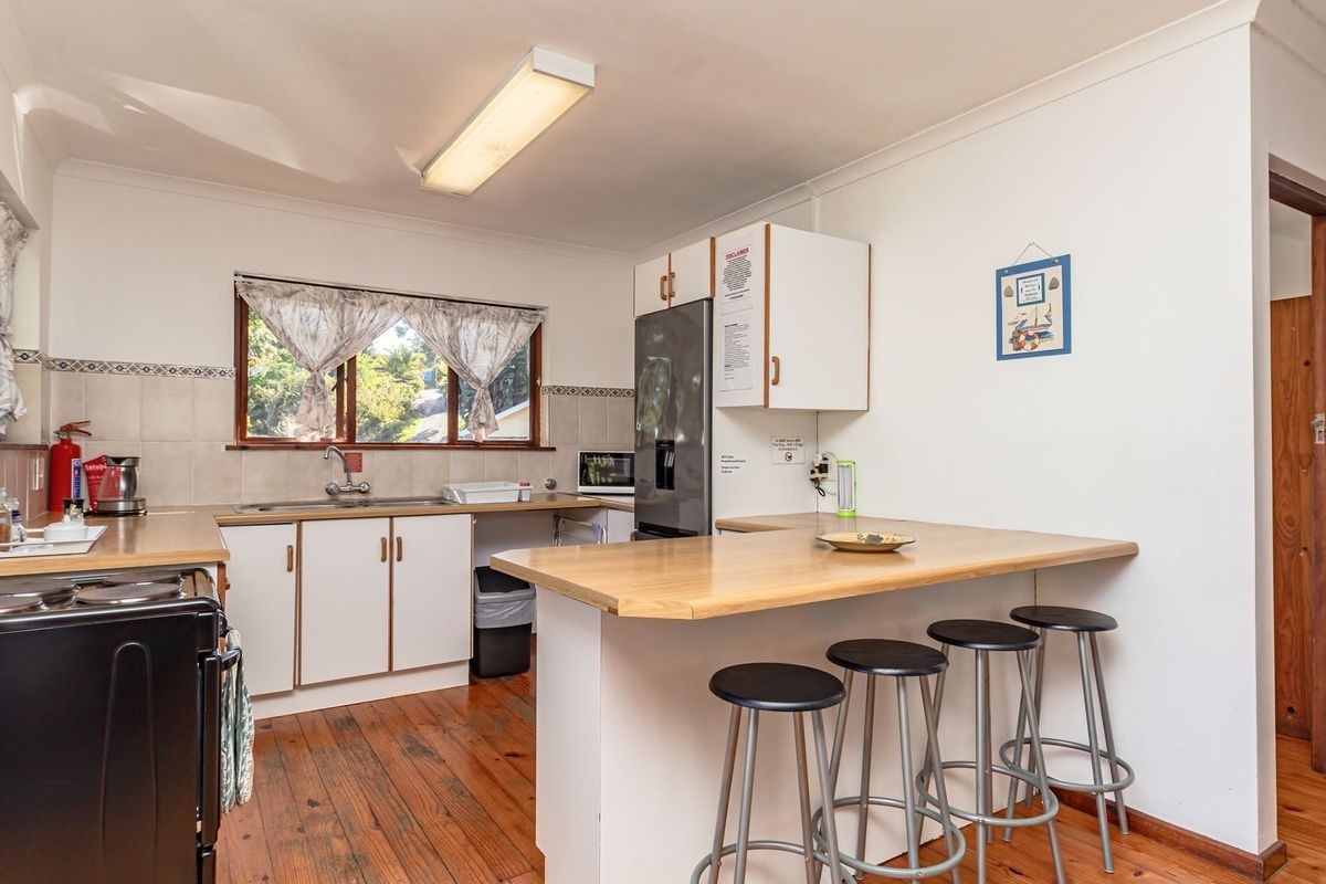 A functional kitchen featuring timber flooring, laminate countertops, a breakfast bar, and built-in cabinetry with a double sink and window views.