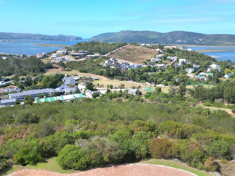 An elevated aerial view showcasing the surrounding residential estate, natural coastal landscape, and scenic water views.
