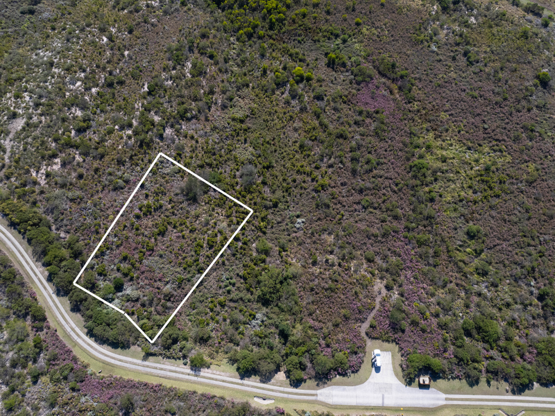 Aerial view of a vacant residential plot featuring natural vegetation and surrounding landscape, clearly demarcated for development.