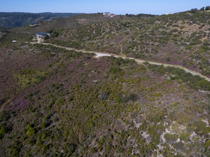 Aerial view of a large, undeveloped residential plot featuring natural vegetation and access to a gravel road in a scenic hillside location.