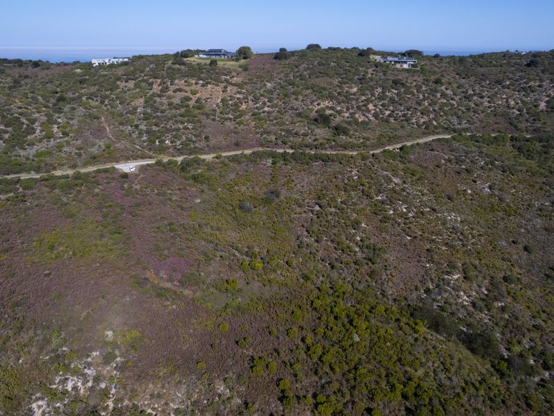 An aerial view of a large, undeveloped residential plot featuring natural coastal vegetation and a dirt access road.